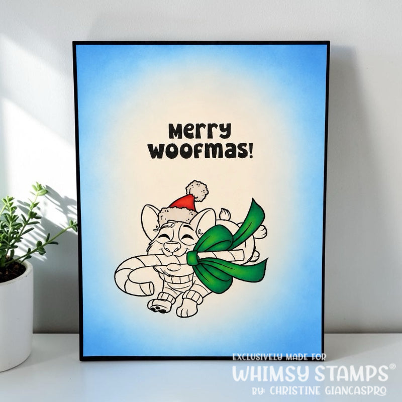 A simple greeting card featuring a cartoon Corgi wearing a Santa hat carrying a candy cane with a large green bow, set against a blue ink blended background with the text 'Merry woofmas!'. 