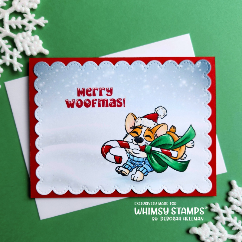 A handmade Christmas greeting card with a red border and scalloped edge, featuring a cartoon dog wearing a Santa hat and holding a candy cane and green gift, with the text 'Merry Woofmas!'. 