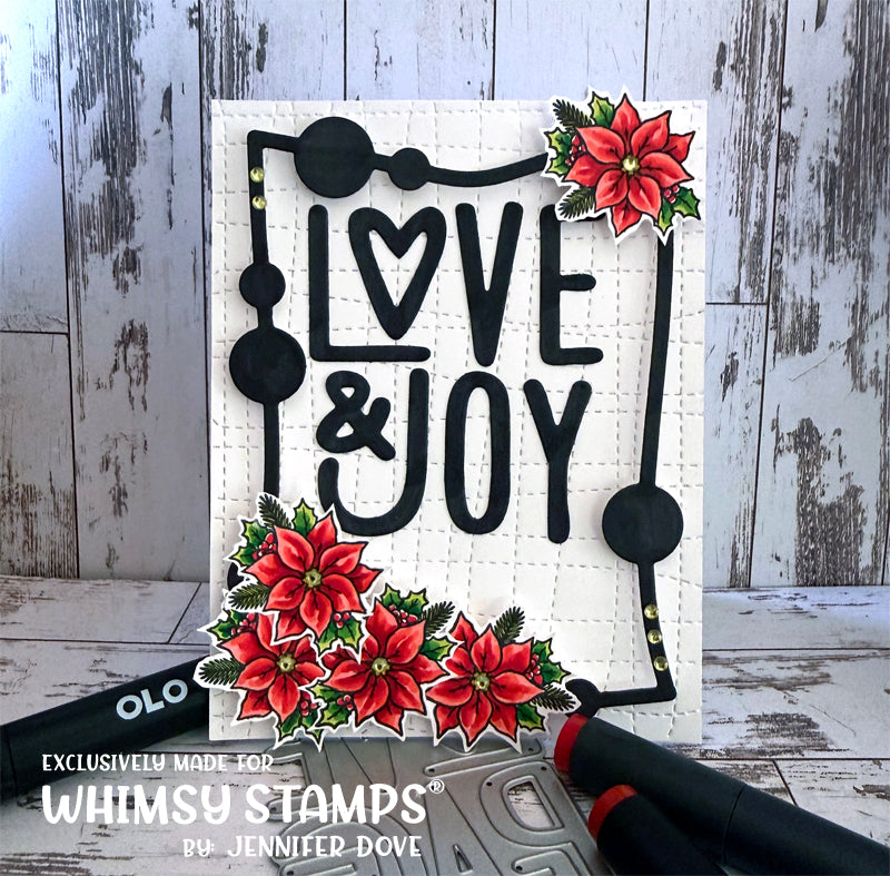 A handmade holiday greeting card featuring the words 'LOVE & JOY' in black lettering with a heart-shaped 'O' and a black decorative border. The card is decorated with red poinsettia flowers and green leaves, set against a rustic white wood background.