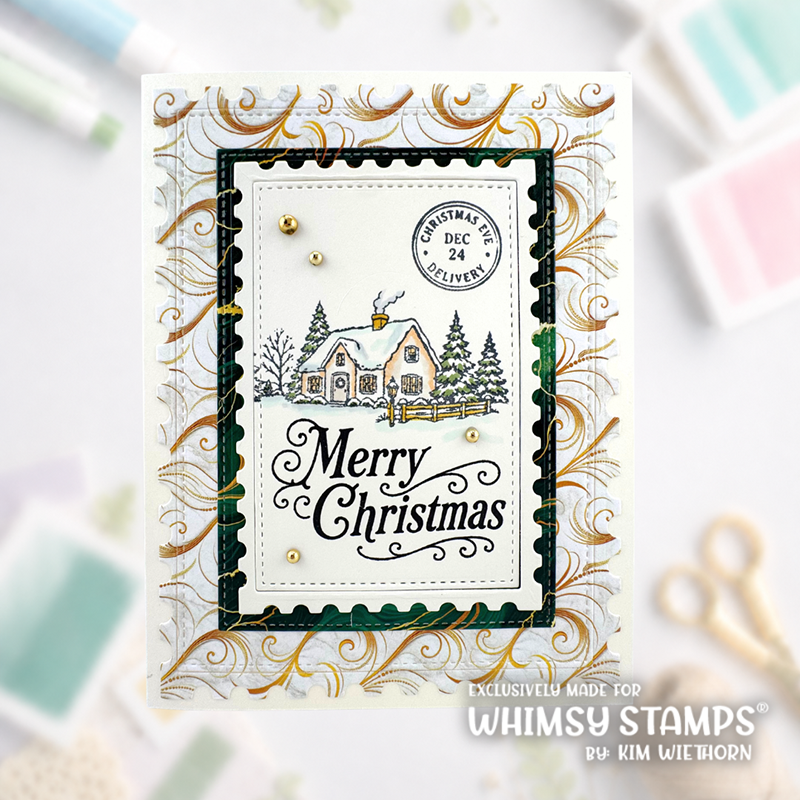 A handmade Christmas greeting card featuring a festive illustration of a cozy house, evergreen trees, and the words 'Merry Christmas' in black script. The card has a layered design with gold and green scalloped borders and small gold pearl accents.