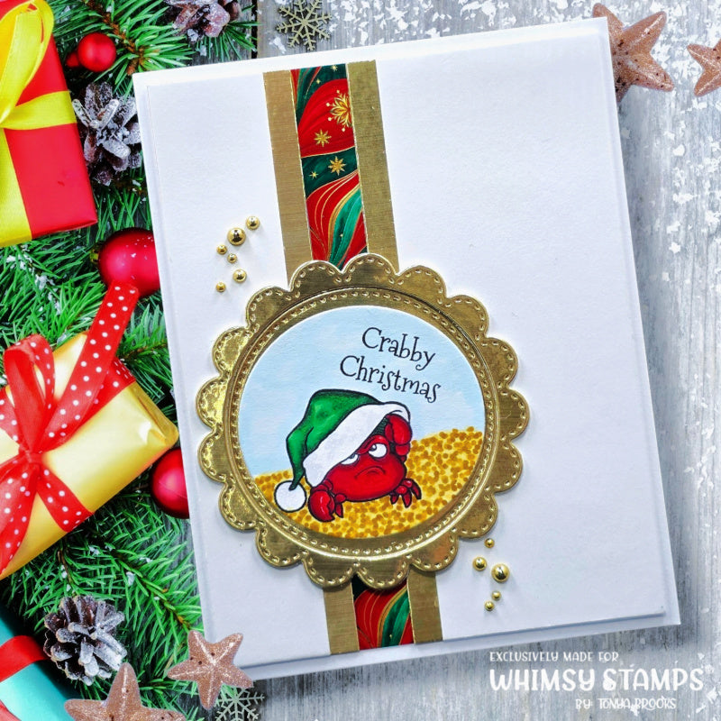 A handmade Christmas greeting card featuring a scalloped gold border with a circular stamp design of a red crab wearing a green Santa hat on a gold background, surrounded by a vertical gold and multicolor ribbon stripe. 