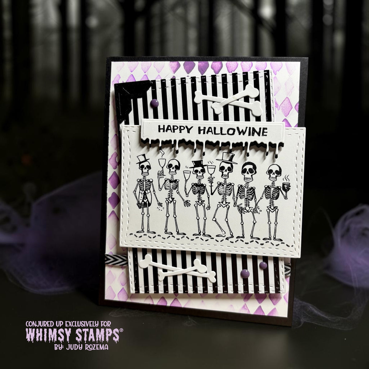 A handmade Halloween card with a line of six skeletons, some wearing top hats and holding wine glasses, above black-and-white striped and purple harlequin backgrounds. A drippy sentiment reads 'Happy Hallowine"